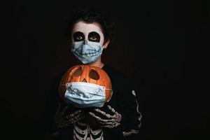 glad halloween, unge med medicinsk mask i en skelettdräkt med halloweenpumpa foto