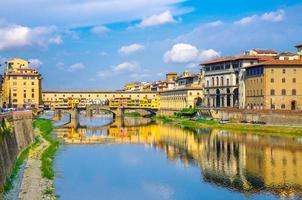 Ponte vecchio bro med färgglada byggnader hus över Arno floden blått reflekterande vatten foto