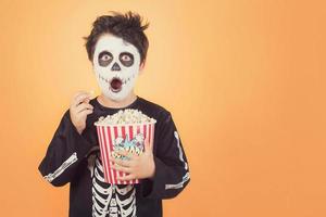 glad halloween. förvånat barn i en skelettdräkt med popcorn foto