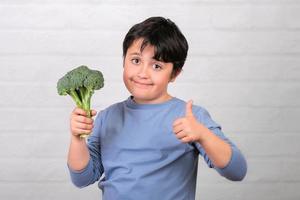 lyckligt barn med broccoli i handen visar tummen up.healthy mat koncept foto