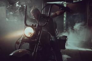 stilig brutal man med skägg som sitter på en motorcykel i sitt garage foto