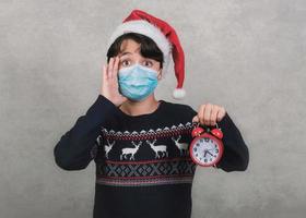 god jul, roligt barn med medicinsk mask och väckarklocka bär jultomten hatt foto