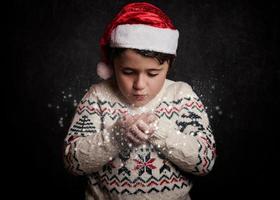 litet barn blåser snö från händerna i jul foto