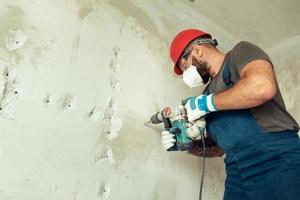 byggare med perforator borrar hål i betongvägg foto