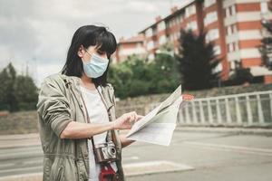kvinna som bär medicinsk mask med en kamera tittar på en karta över staden foto