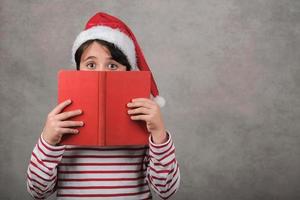 god jul, nyfiket barn som bär jultomtenhatt med bok foto