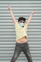glad unge som bär medicinsk mask hoppar på gatan foto