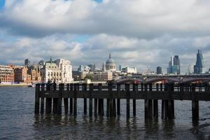 vacker utsikt över london skyline från flodstranden. gammal träpir, saint paul katedral och skyskrapor. molnig dag, solnedgång. foto