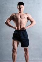 muskulös asiatisk man poserar på grå bakgrund foto