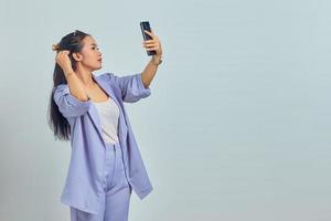 porträtt av ung asiatisk kvinna som gör hennes hår medan du ringer videosamtal på vit bakgrund foto