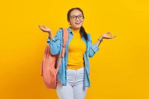 ung asiatisk student i jeanskläder med ryggsäck hålla händerna i yoga om aum gest slappna av meditera försök att lugna ner isolerad på gul bakgrund. utbildning i gymnasiekonceptet foto