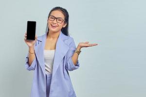 porträtt av glad ung asiatisk kvinna som presenterar kopia utrymme och håller smartphone isolerad på vit bakgrund foto
