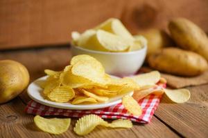 potatischipssnacks på vit tallrik, krispiga potatischips på köksbordet och färsk råpotatis foto