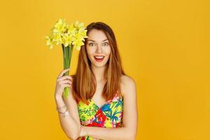 kvinna som håller gula blommor och hon blir förvånad mot gul vägg foto