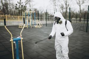 rengöring och desinfektion på lekplatsen i stadskomplexet mitt i coronavirusepidemiteam för desinfektionsinsatser infektionsförebyggande och kontroll av epidemiskyddsdräkt och mask foto