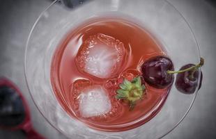 ett glas röd cocktail med sommarfrukt foto