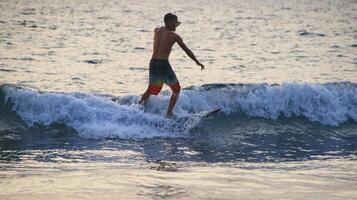 dokumentation av surfare i aktion i skymningen med en gyllene färg och mörk, ofokuserad och mörk på stranden i senggigi lombok, västra nusa tenggara, Indonesien, 27 november 2019 foto