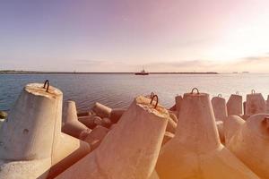 fartyg-bogserbåt går i öppet hav för att bogsera lastfartyg till hamn, vacker solnedgång över piren, tetrapod vågbrytare i hamnen. foto