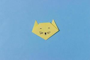 kattens huvud är vikt från gult papper i tekniken för origami med målade ögon, näsa och mustasch. i mitten av den blå bakgrunden. foto