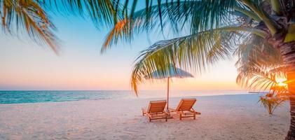 panoramautsikt tropisk strand solnedgång strålar, två solstolar, solstolar, parasoll under palmträd. vit sand, havshorisont, färgglad skymningshimmel, lugn slappna av banner. inspirerande strandhotell foto