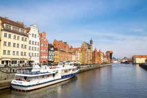 gdansk, Polen, 15 april 2018 vitt turistbåtsfartyg på motlawaflodens vatten, typiska färgglada husbyggnader och zuraw-kran vid långa brovallens strandpromenadgata i historiska centrum foto