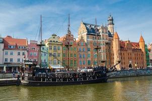 gdansk, Polen, 15 april 2018 medeltida träturistfartyg på motlawaflodens vatten, typiska färgglada husbyggnader vid långa brovallens strandpromenadgata i hamnen i den historiska stadskärnan foto