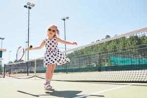 söt liten flicka spelar tennis på tennisbanan utanför foto