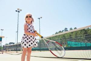 söt liten flicka spelar tennis på tennisbanan utanför foto