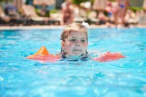 flicka simmar i poolen i armband på en varm sommardag. foto