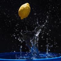 saftig gul citron faller i vatten på en svart bakgrund foto