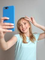 snygg vacker blond kvinna bloggare gör selfie med sin smartphone vid fönstret. trend, teknik, skönhet, modekoncept foto