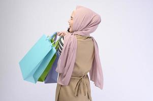 ung vacker muslimsk kvinna i kostym håller färgglada shoppingkassar över vit bakgrund studio foto