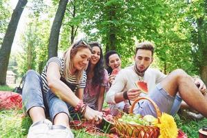 grupp vänner som har picknick i en park en solig dag - folk umgås, har roligt medan de grillar och kopplar av foto