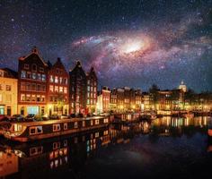 vacker natt i amsterdam. nattbelysning av byggnader och båtar nära vattnet i kanalen. med tillstånd av nasa foto