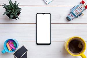 kreativt arbetsbord platt liggande komposition med smart telefonmockup omgiven av robotleksak, kaffemugg, växt och färgad krita foto