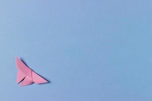 rosa origami fjäril viker ut ur papper. blå bakgrund med kopia utrymme. utbildning, tidsfördriv, fritidsintressen, aktiviteter med barn. minimalistisk bakgrund foto