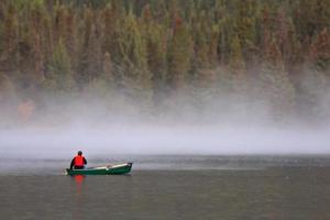 man i kanot nära morgondimma på sjön foto