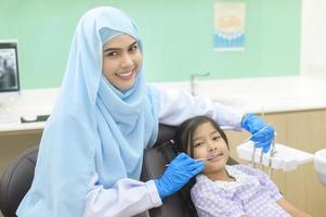 en liten söt flicka som har tänder undersökta av muslimsk tandläkare på tandklinik, tandkontroll och friska tänder koncept foto