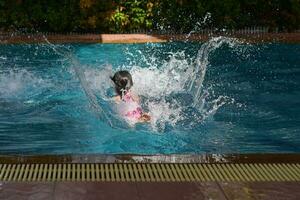liten flicka hoppar i poolen på en sommardag, stort plask. foto