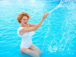 leende rödhårig kvinna porträtt njuter av livet i vit simdräkt i poolen foto