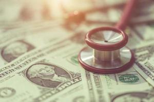 rött stetoskop på amerikanska dollar sedeln på träbord. hälsokontroll eller pengar och finansiellt koncept foto