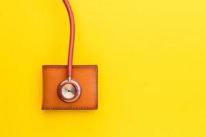 läkarestetoskop och den nya bruna läderplånboken för män på gul bakgrund. budget för hälsokontroll eller pengar och ekonomiskt koncept foto