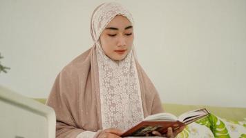 vacker muslim som läser koranen sittandes i soffan foto