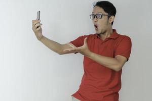 wow ansikte av ung asiatisk man chockade vad han ser i smartphone på isolerad grå bakgrund. foto