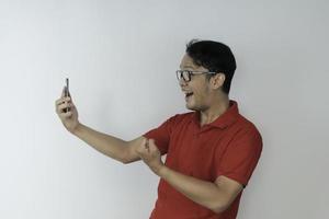 ung asiatisk man chockad och nöjd med vad han ser i smartphonen på isolerad grå bakgrund. foto