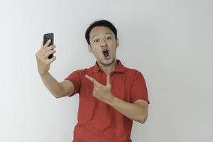 wow ansikte av ung asiatisk man chockade vad han ser i smartphone på isolerad grå bakgrund. foto