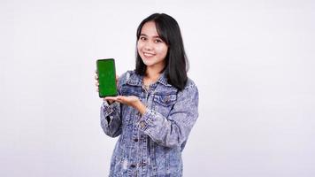 asiatiska kvinnor ler bär jeansjacka och håller grön skärm telefon med isolerade vit bakgrund foto