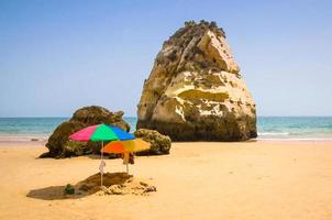 akvarellteckning av två färgade parasoller på stranden, portugal, algarve, barnsandlåda på stranden, enorma stenar på havsstranden foto