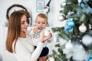 lycklig familj mor och bebis dekorerar julgran foto