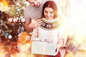 ungt par firar jul. en man gav plötsligt en present till sin fru. begreppet familjelycka och välbefinnande. bokeh ljus mjuk effekt foto